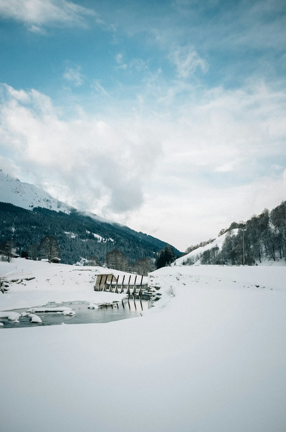 snow covered field and mountains under white clouds and blue sky during daytime