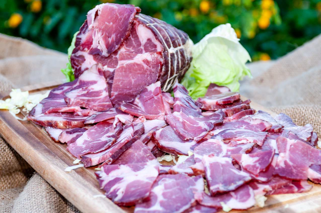 Close-up of a skilled hand slicing thin, translucent slices of Iberian acorn-fed ham on a wooden board.