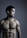 A shirtless man with a muscular physique stands against a dark gray background. His head is slightly turned to the side, eyes closed, exhibiting a calm and contemplative expression. The lighting emphasizes the contours of his body, highlighting his well-defined muscles.
