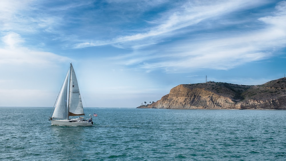 white sailboat on sea near brown rock formation under blue sky during daytime