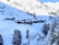 A snowy alpine landscape with a cluster of wooden cabins nestled at the base of a mountain. Snow-covered slopes and pine trees surround the area, creating a serene and picturesque scene. The bright sunlight casts shadows on the hillside, adding depth to the tranquil setting.