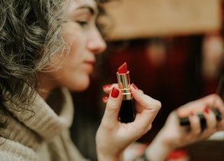 woman in gray sweater holding lipstick