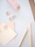A pastel-themed stationery flat lay including a pink stapler, spiral paper clips, paint swatches labeled as 'Soft Marshmallow', a wooden pencil, and a light pink ruler on a white surface.