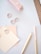 A pastel-themed stationery flat lay including a pink stapler, spiral paper clips, paint swatches labeled as 'Soft Marshmallow', a wooden pencil, and a light pink ruler on a white surface.