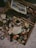 An assortment of scattered, vintage film boxes and booklets is spread out on a flat surface. A newspaper with colorful advertisements is partially visible in the upper section. Various small objects, possibly related to photography, are interspersed among the film boxes.