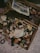 An assortment of scattered, vintage film boxes and booklets is spread out on a flat surface. A newspaper with colorful advertisements is partially visible in the upper section. Various small objects, possibly related to photography, are interspersed among the film boxes.
