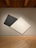 A minimalist art piece displayed on a gallery wall. The artwork consists of two large, overlapping geometric panels, one black and one white, positioned diagonally against a neutral background. The room features wooden floors and a ceiling with visible beams.