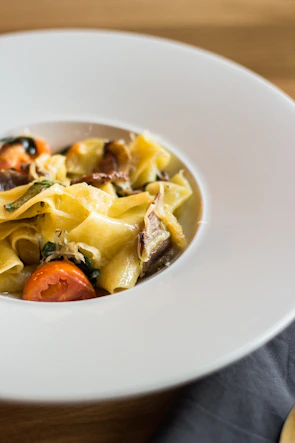 A vibrant bowl of tomato-red penne pasta garnished with fresh basil, styled with clean, modern plating on a dark charcoal surface.