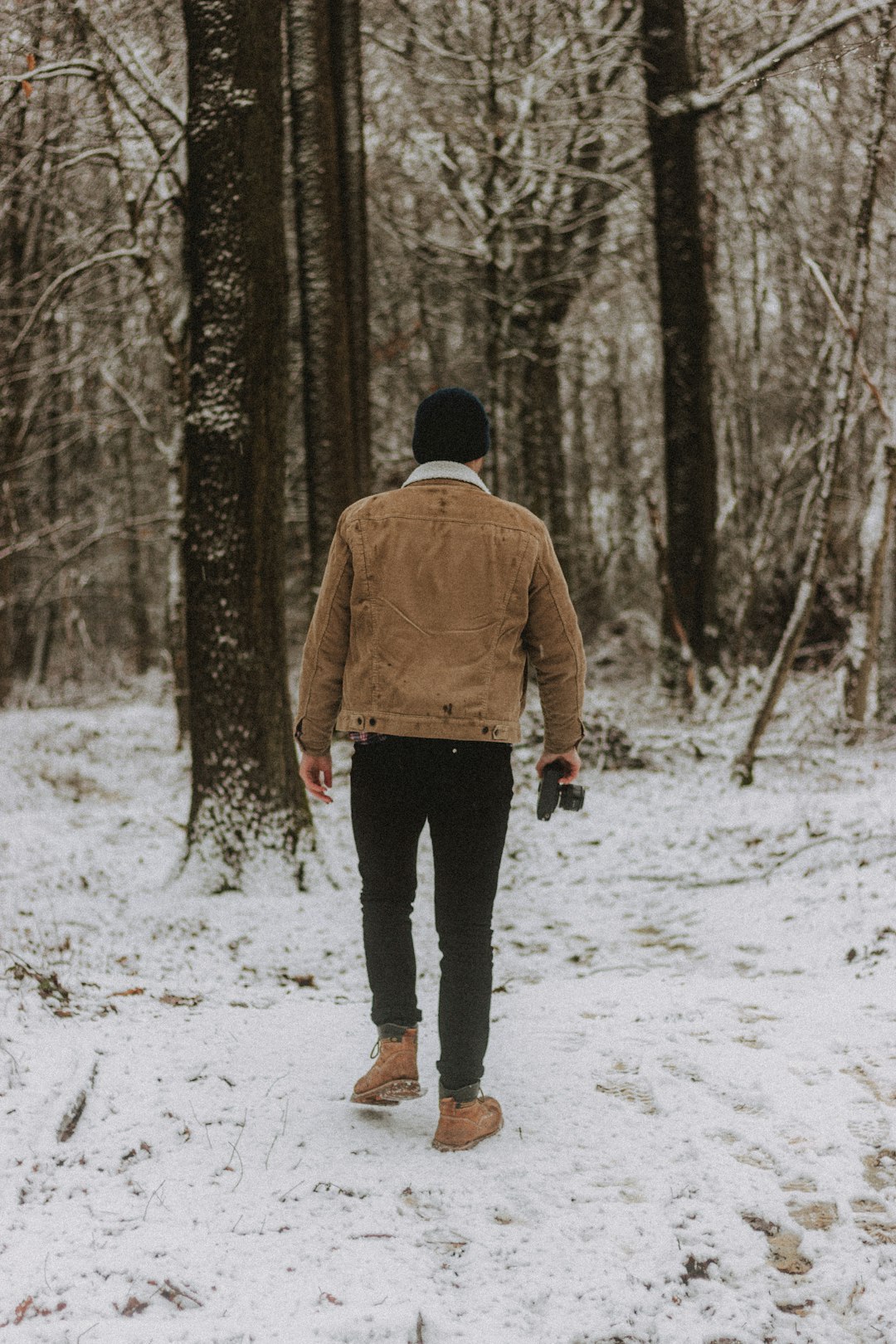 man in brown jacket and black pants walking on snow covered ground during daytime