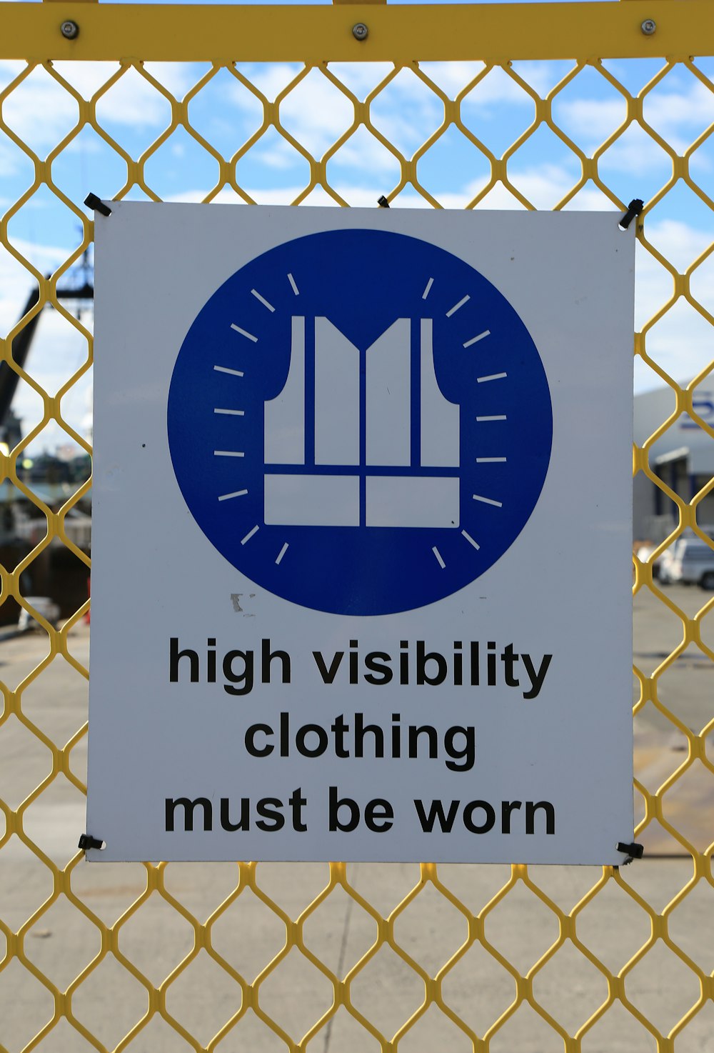 ein Schild an einem Maschendrahtzaun, das besagt, dass Warnkleidung getragen werden muss