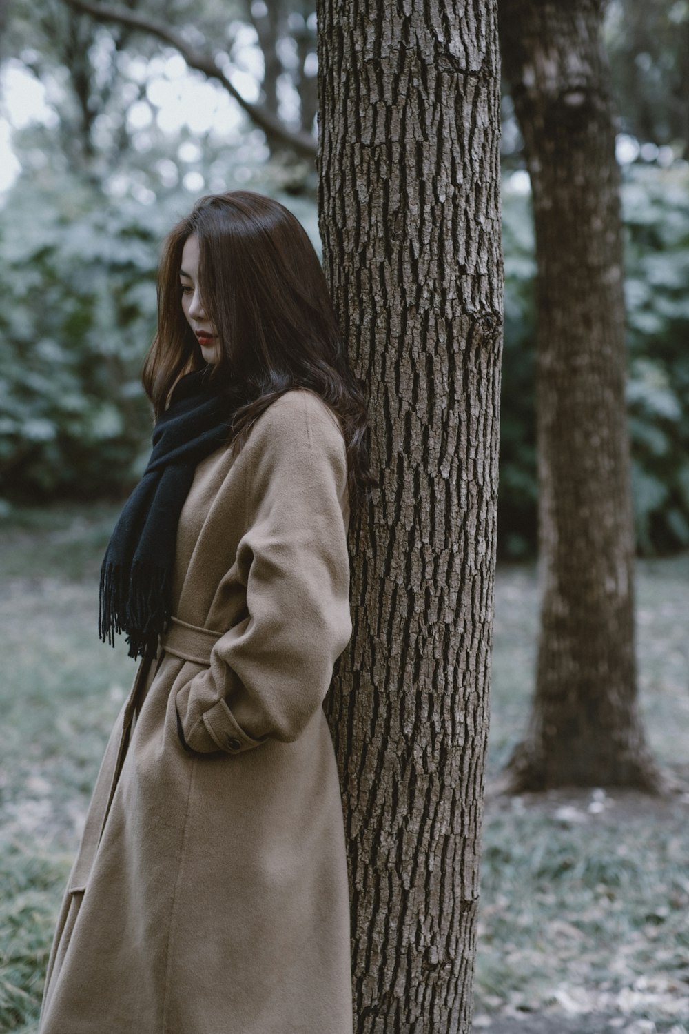 woman in brown coat standing beside brown tree during daytime
