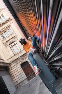 man in orange t-shirt and blue denim jeans sitting on black metal staircase