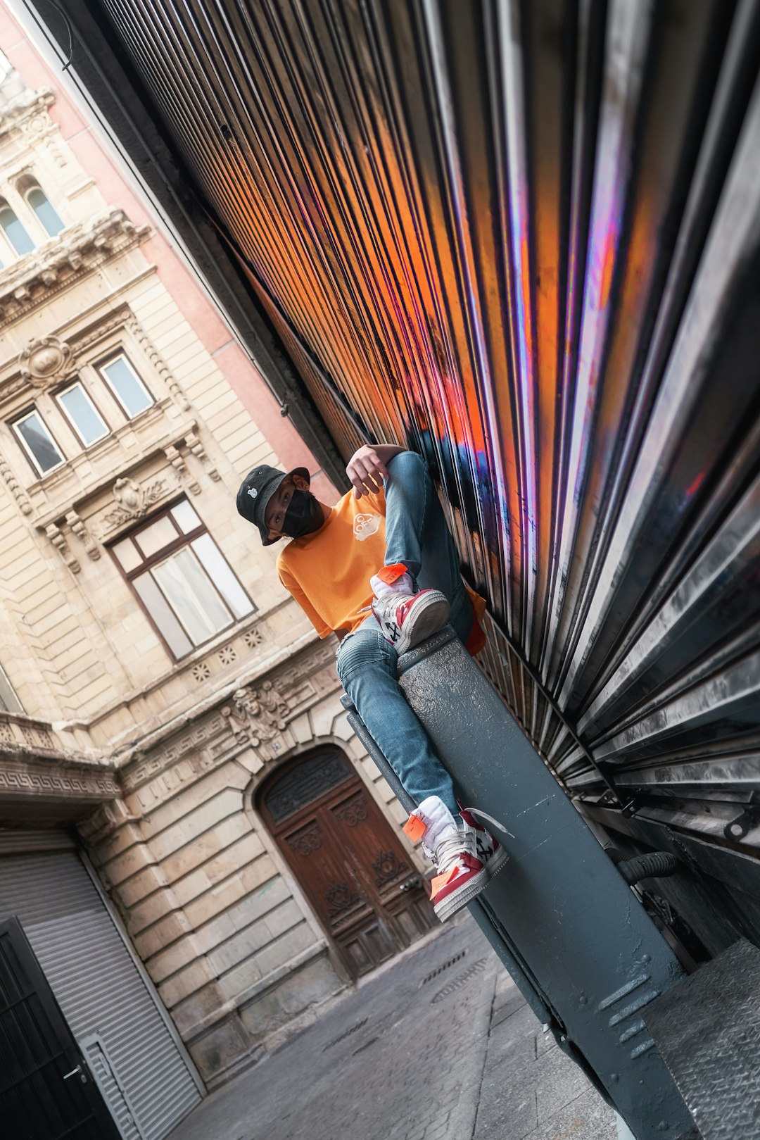 man in orange t-shirt and blue denim jeans sitting on black metal staircase