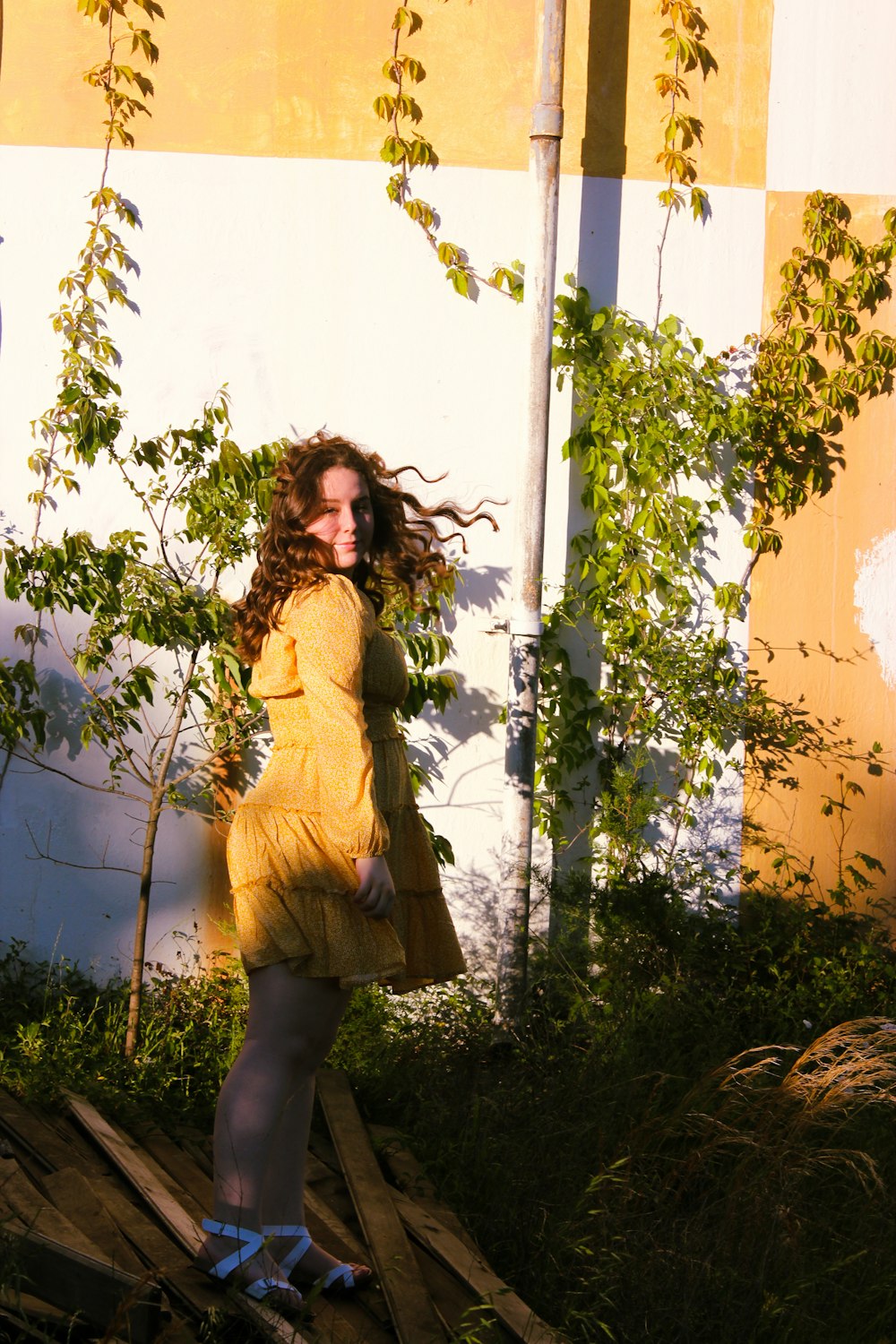 woman in yellow long sleeve shirt and black pants standing beside white wall