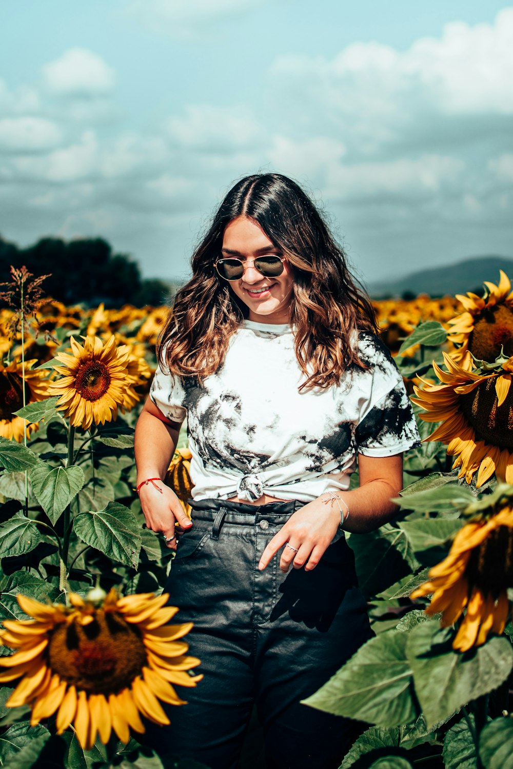 woman in white and black floral shirt standing on sunflower field during daytime
