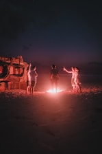 Group of happy surfers relaxing around a bonfire on the beach at sunset.
