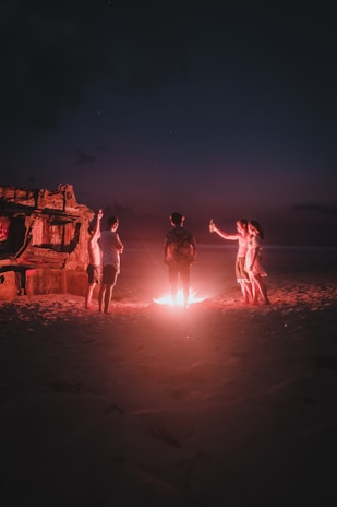 Group of friends enjoying Rocky Brewing beers around a bonfire on the beach at night.