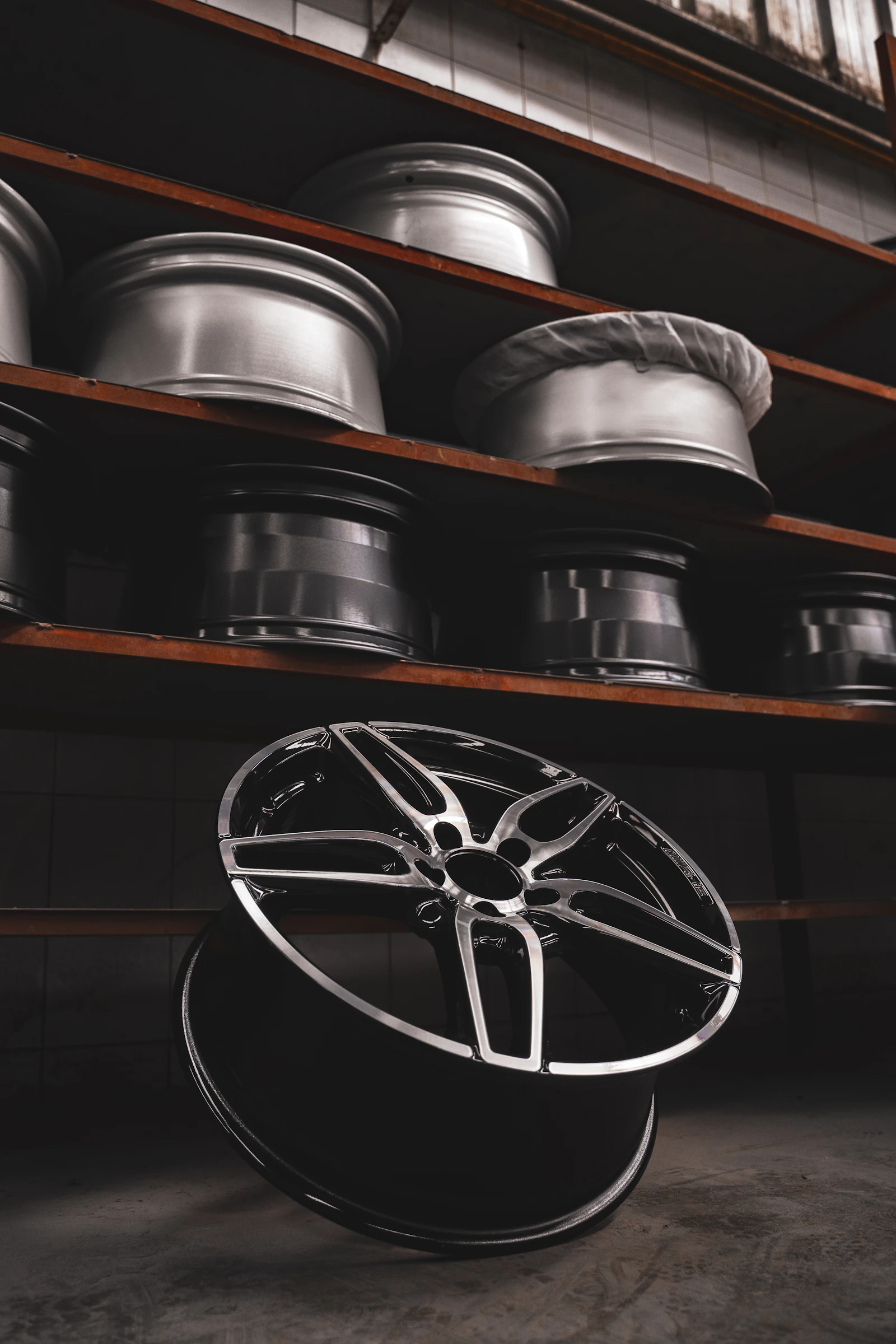 Bare alloy wheels racked in a workshop, with a freshly refinished diamond-cut wheel standing on the floor in front of them.