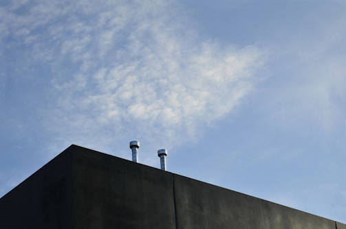 A building corner with two metal pipes extending from the rooftop against a partially cloudy sky.