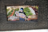 A person stands with a shopping cart in a grocery store, reading a colorful brochure. The store features an array of fresh produce, including leafy greens and root vegetables displayed on shelves. The atmosphere is busy and colorful, indicating a bustling market environment.