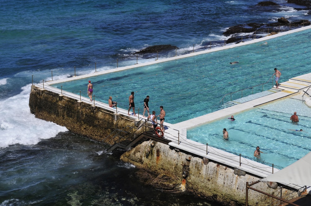 Personas de pie en un puente de concreto blanco cerca del cuerpo de agua durante el día