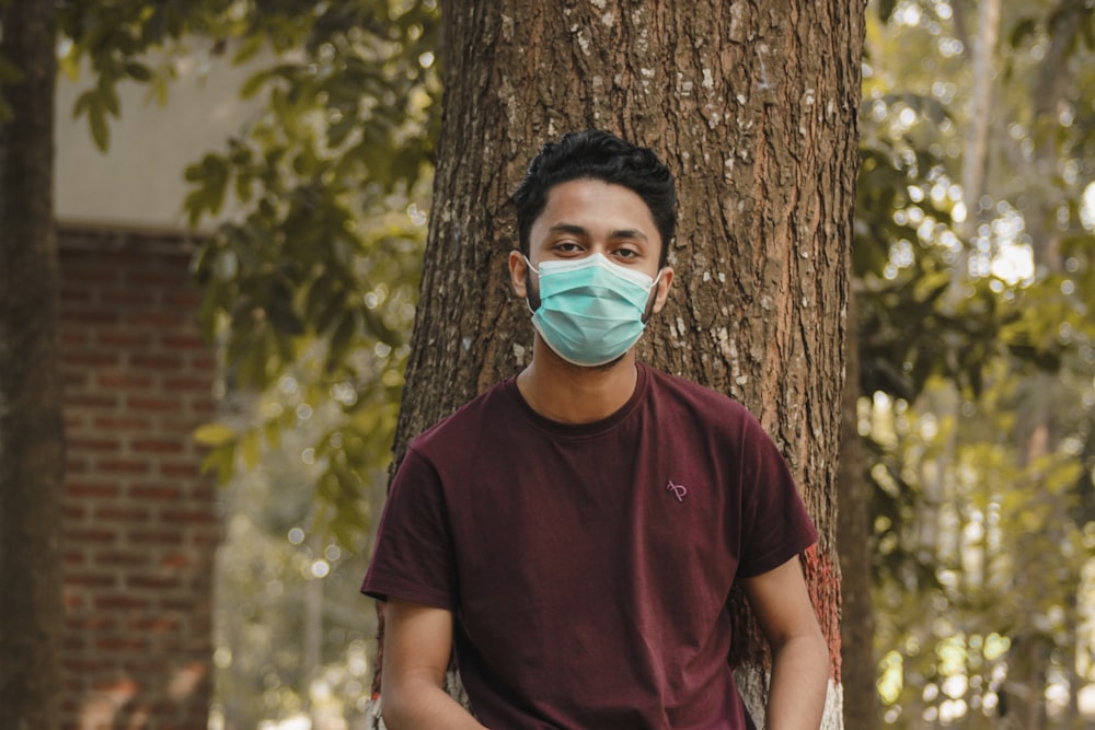 Uomo in t-shirt girocollo marrone con maschera facciale in piedi accanto all'albero marrone durante il giorno