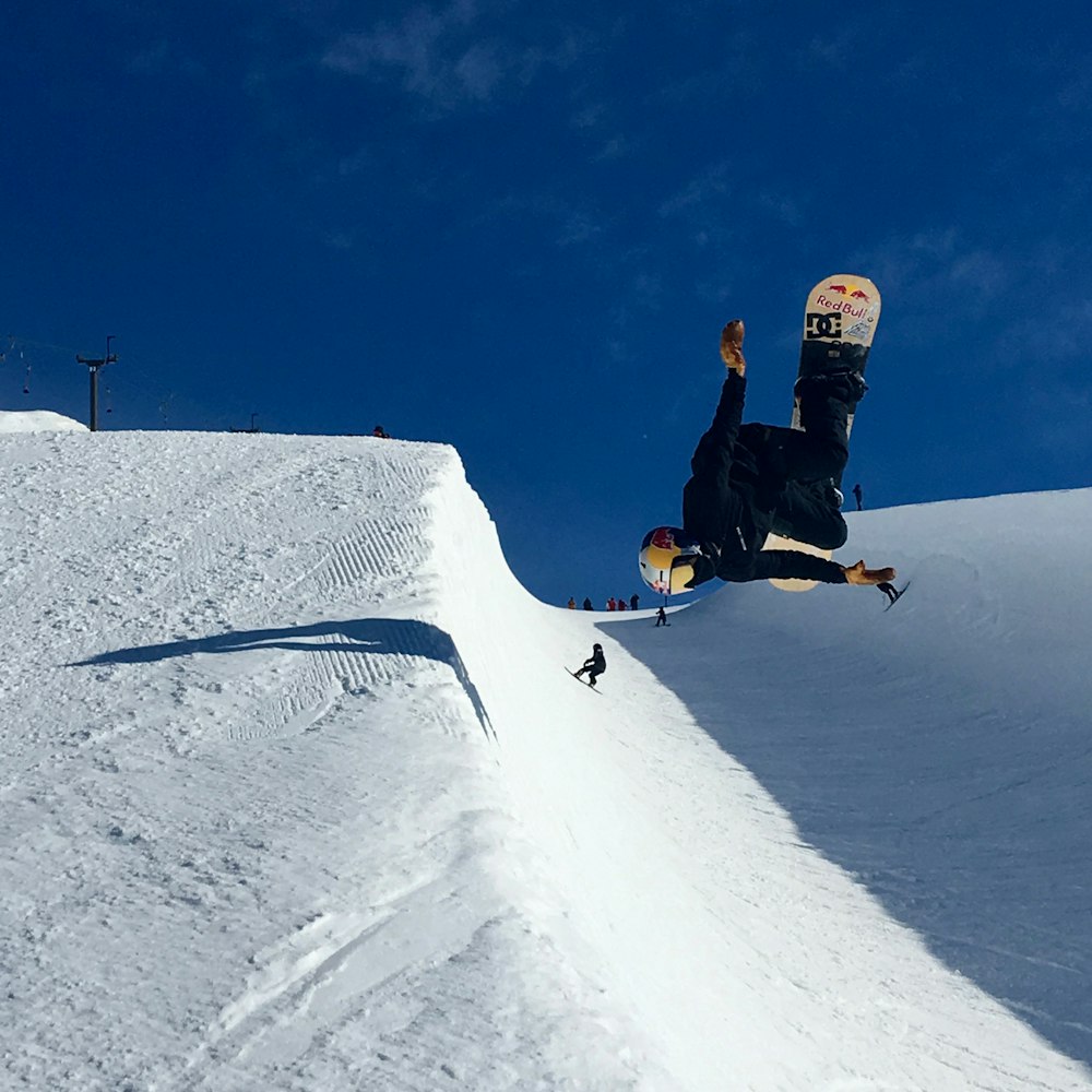 man in black jacket and black pants riding on yellow snowboard on snow covered ground during