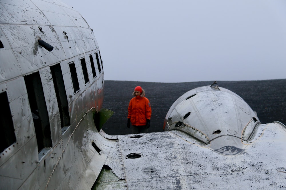 man in red jacket standing beside white airplane