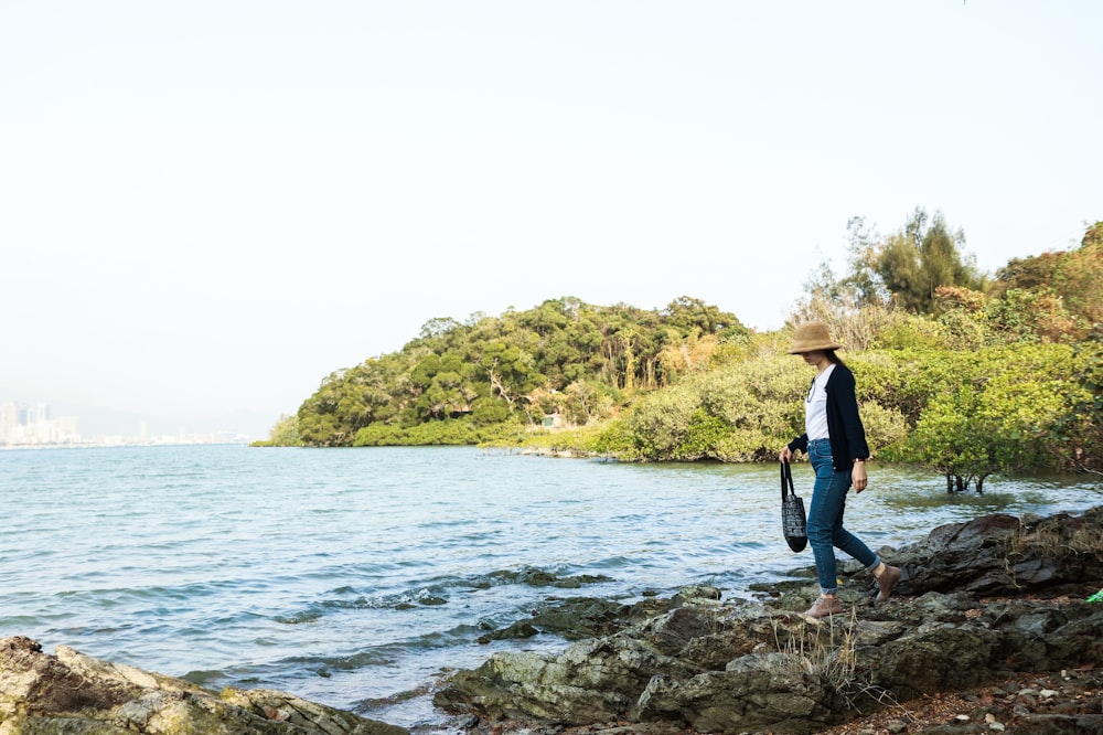 woman in black shirt and blue denim jeans standing on rocky shore during daytime