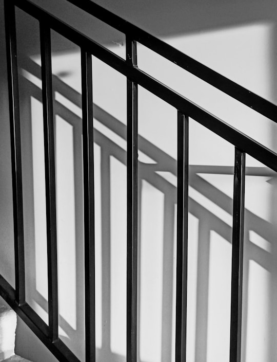 Black metal railing casting distinct shadows against a white wall, creating a play of light and shadow.