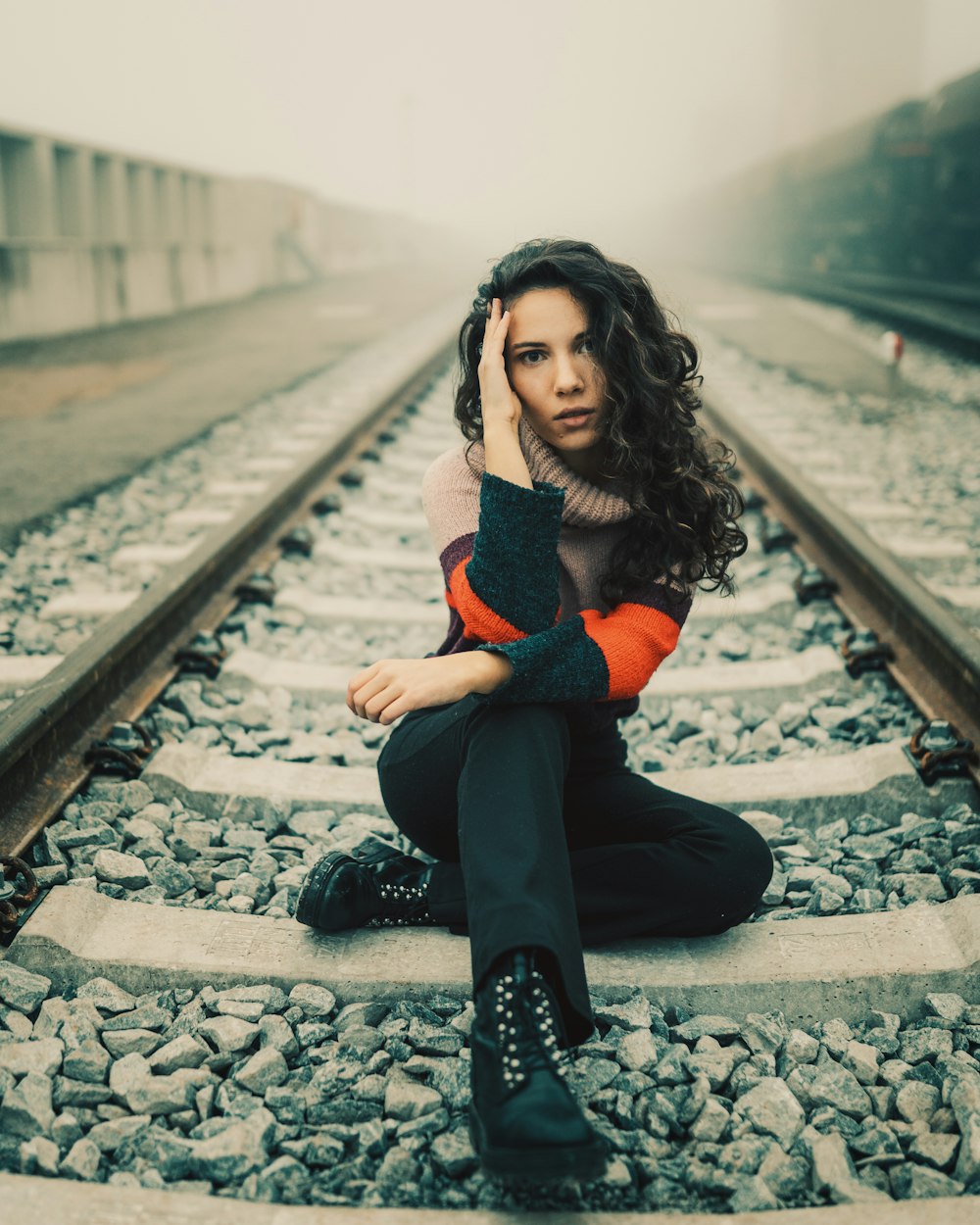 woman in black and orange long sleeve shirt sitting on train rail during daytime
