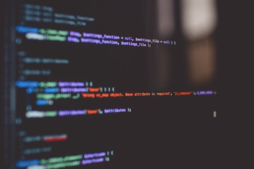 Lines of code are displayed on a dark computer screen, featuring various colored syntax highlighting including green, blue, purple, and red against a black background.