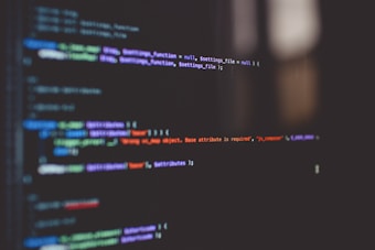 Lines of code are displayed on a dark computer screen, featuring various colored syntax highlighting including green, blue, purple, and red against a black background.