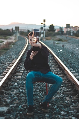 A hand holding a guitar neck resting on a train seat, with blurred countryside passing by.