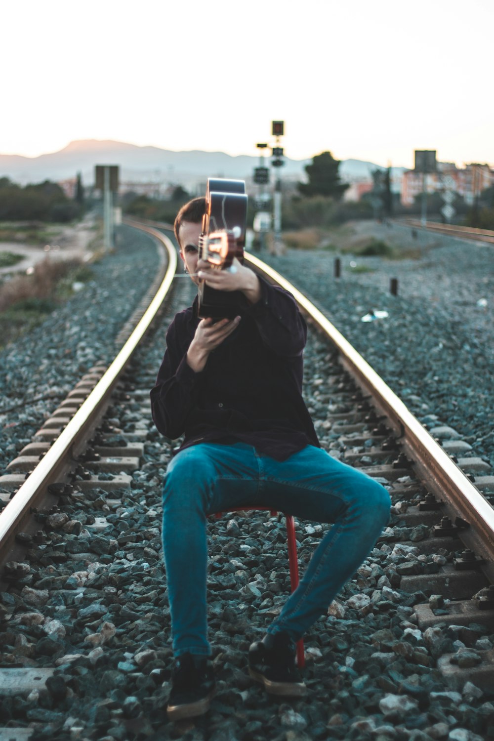 woman in black long sleeve shirt and blue denim jeans sitting on train rail during daytime