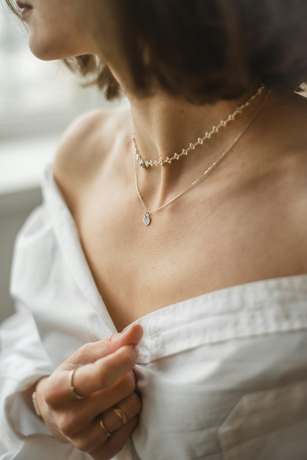 Mujer en camisa blanca con hombros descubiertos con collar plateado