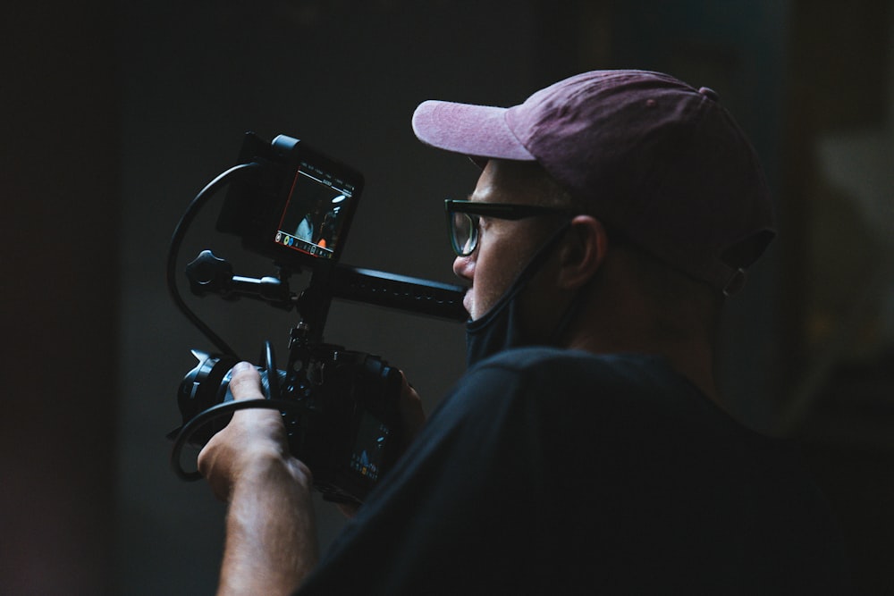 man in black shirt and brown hat holding black video camera