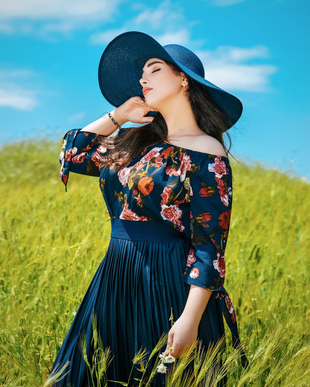 woman in blue and red floral dress wearing black hat standing on green grass field during