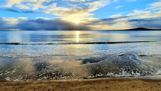 A serene beach at sunset with calm waves and a clear sky.