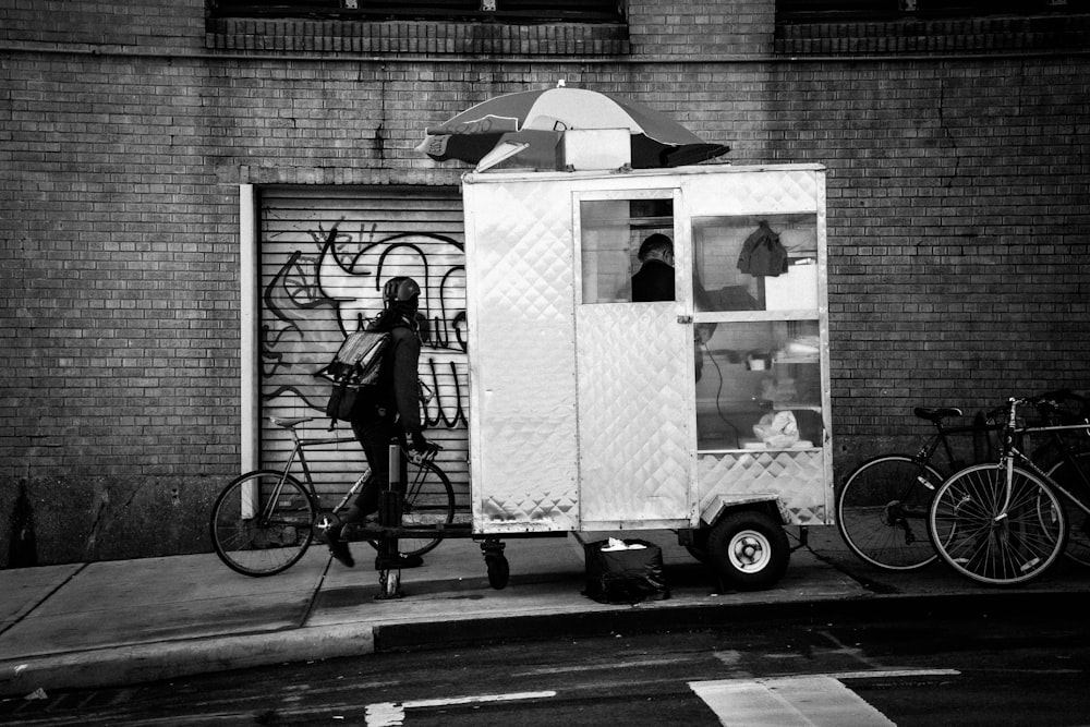 mulher na jaqueta preta que monta na bicicleta na fotografia em tons de cinza