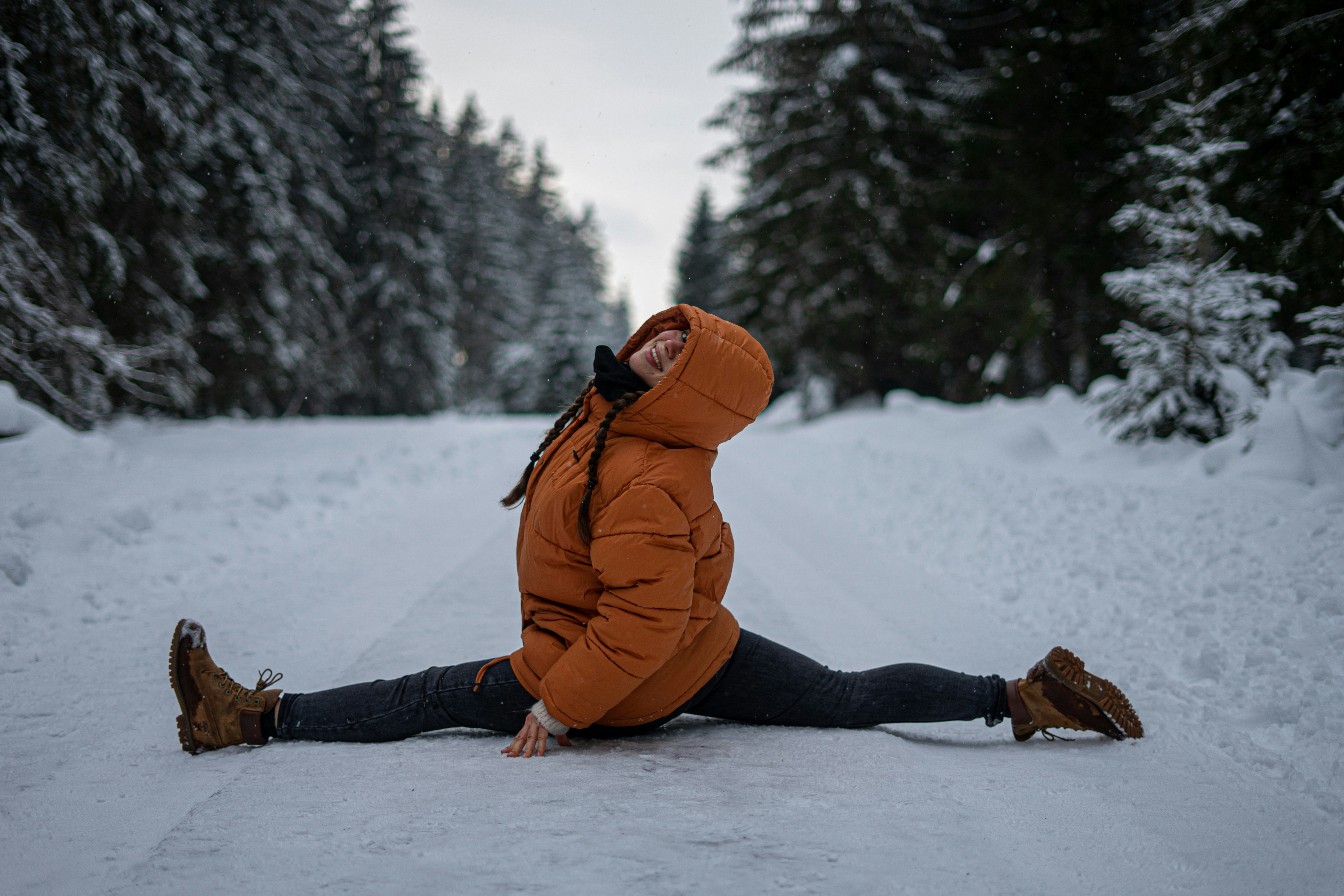 woman in orange jacket and black pants sitting on snow covered ground during daytime