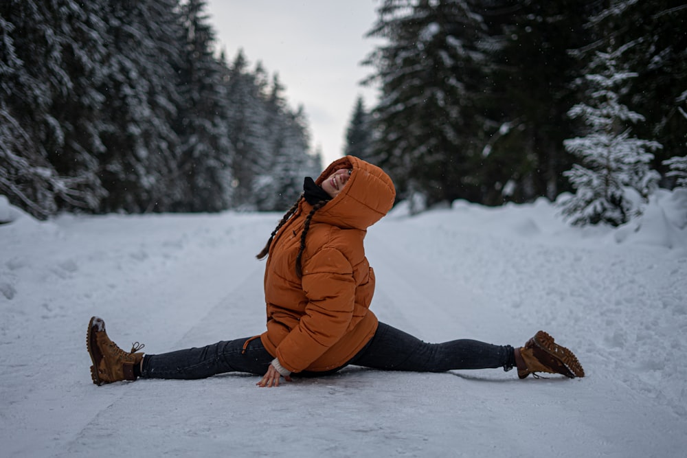 woman in orange jacket and black pants sitting on snow covered ground during daytime