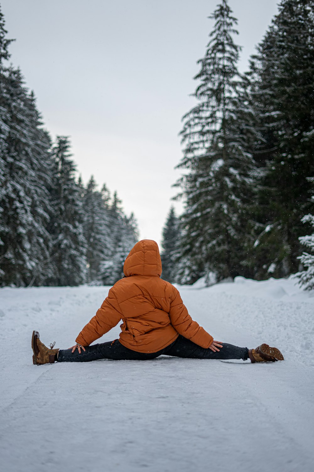 person in orange hoodie sitting on snow covered ground during daytime