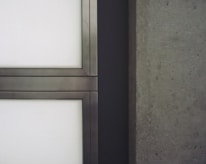 A close-up view of a modern architectural element featuring metal-framed glass panels on the left and a textured concrete wall on the right.