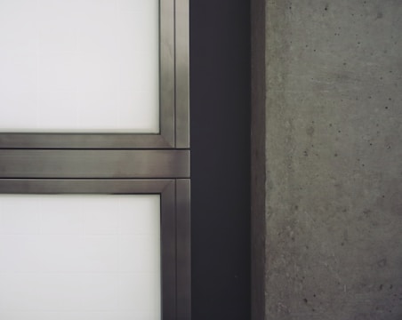 A close-up view of a modern architectural element featuring metal-framed glass panels on the left and a textured concrete wall on the right.