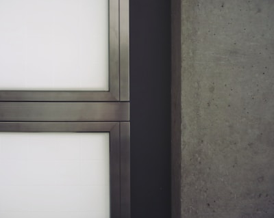 A close-up view of a modern architectural element featuring metal-framed glass panels on the left and a textured concrete wall on the right.