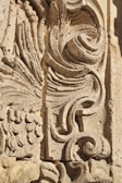 Detailed stone carving with intricate swirling and floral patterns, showcasing expert craftsmanship. The texture and shadowing create depth and highlight the artistic features.
