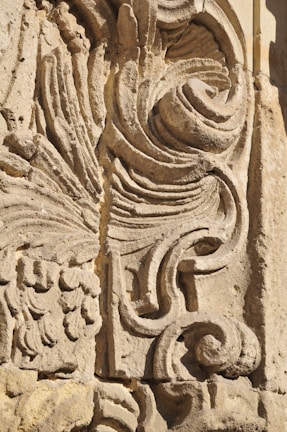 Detailed stone carving with intricate swirling and floral patterns, showcasing expert craftsmanship. The texture and shadowing create depth and highlight the artistic features.