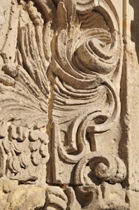 Detailed stone carving with intricate swirling and floral patterns, showcasing expert craftsmanship. The texture and shadowing create depth and highlight the artistic features.