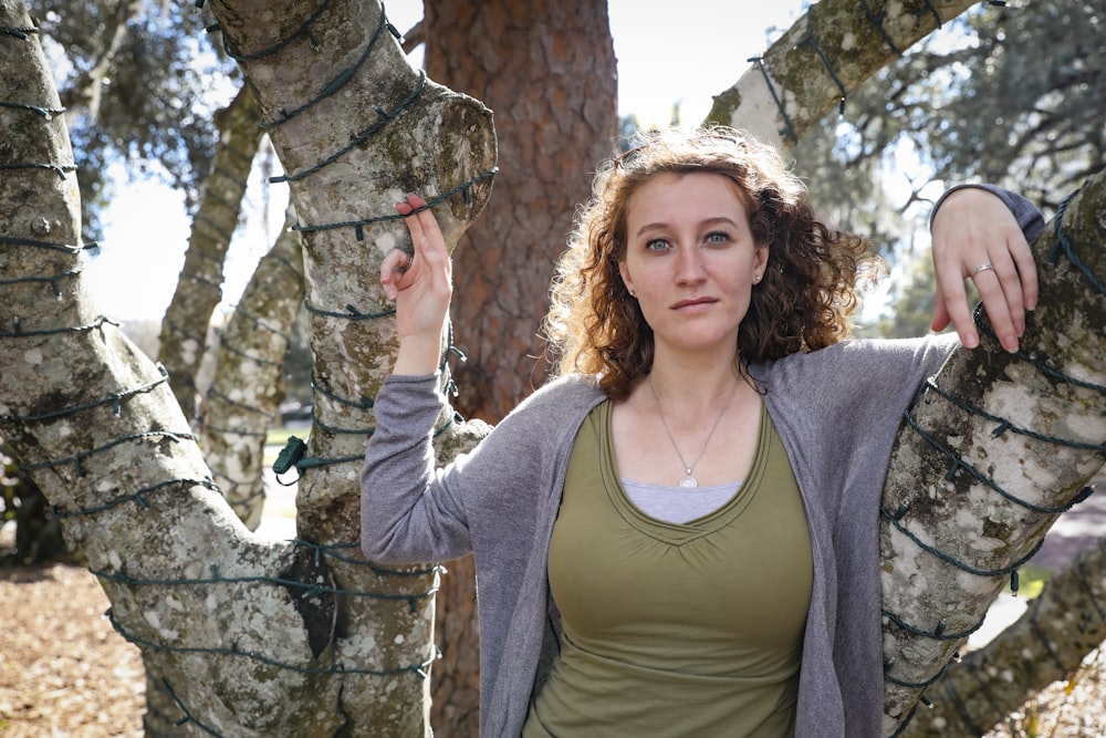 woman in gray scoop neck long sleeve shirt standing beside brown tree during daytime